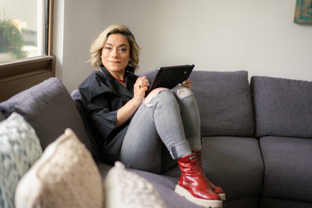 La mentora Hilse Peralta se encuentra sentada en un sillón gris, con una tableta en la mano. Ella puede ayudarte a desarrollar la toma de decisiones efectivas.